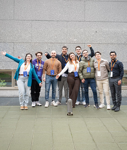 A group of smiling people wearing lanyards pose for a group photo in front of a building.